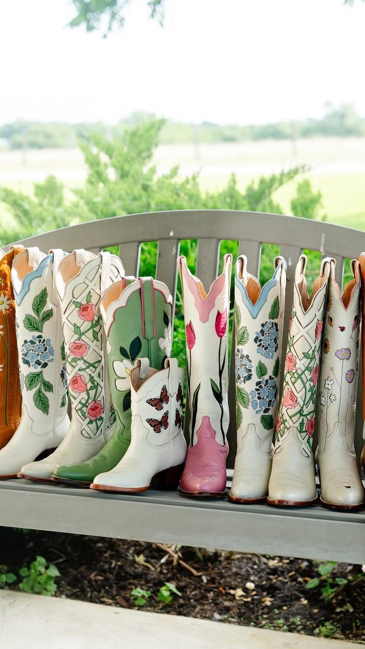 White cowboy boots with colorful floral embroidery lined up on a grey bench.