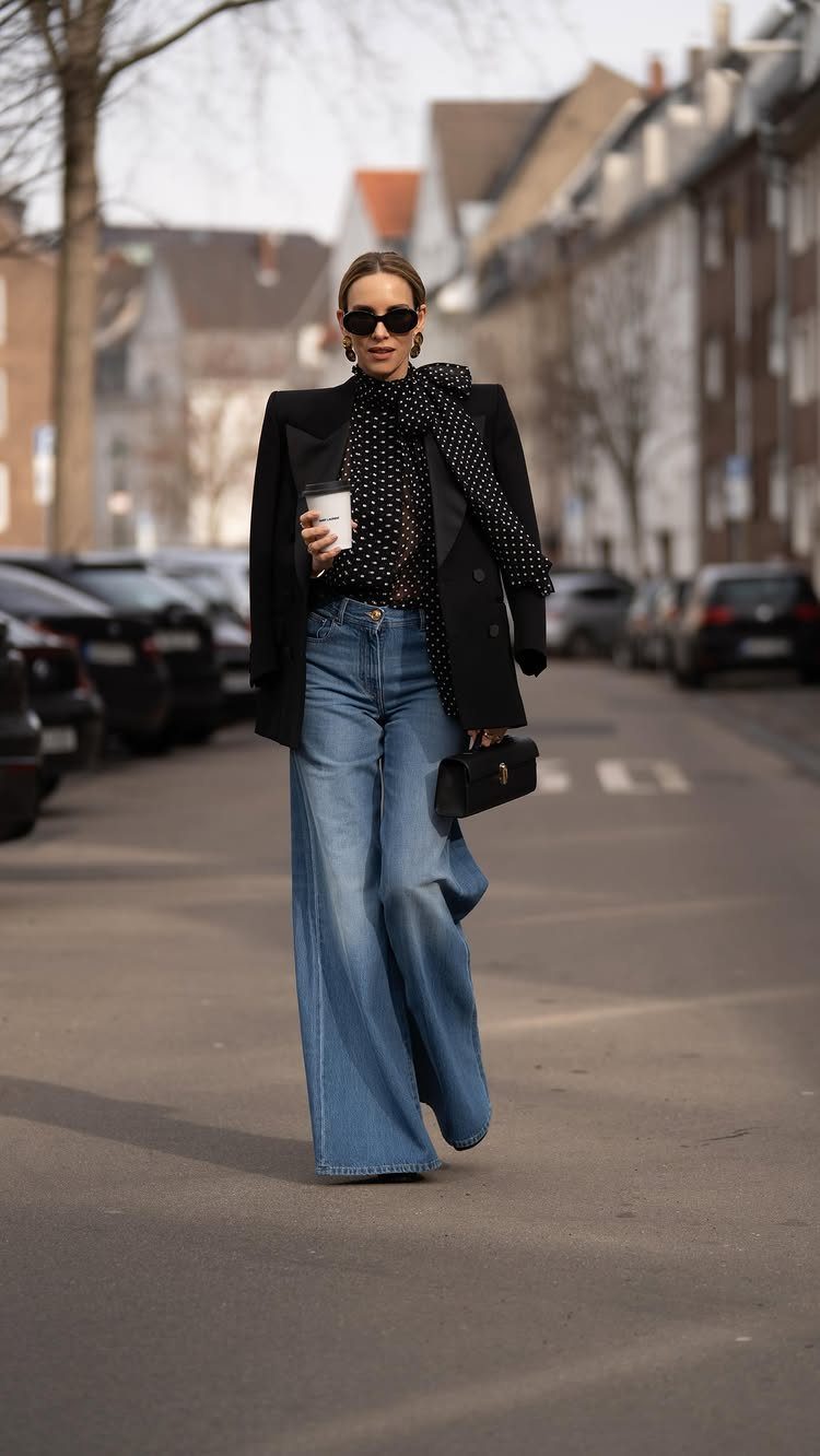 Woman in a black blazer and wide-leg blue jeans walking on a city street