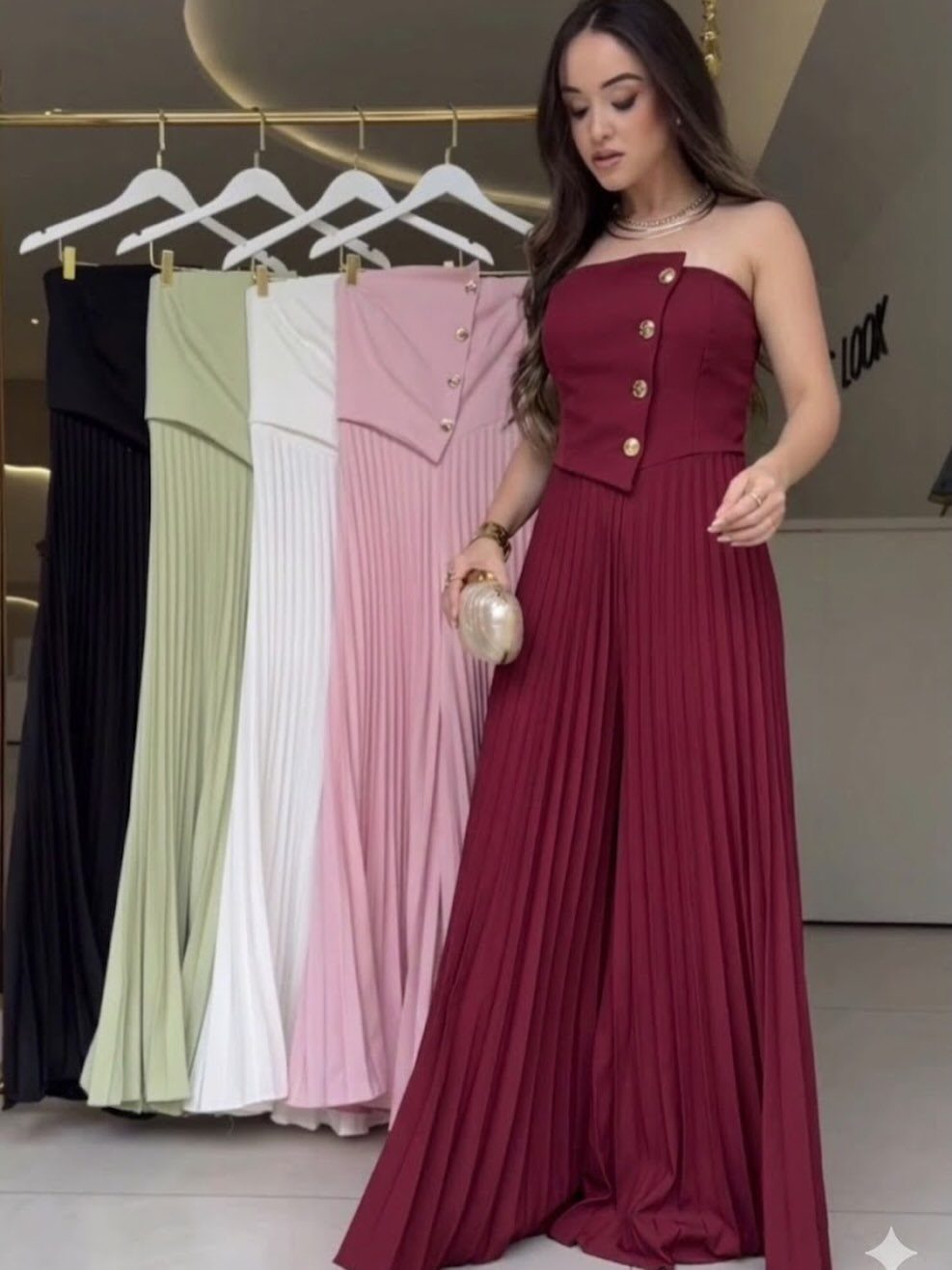 Woman in a strapless burgundy pleated jumpsuit standing before a clothing rack.