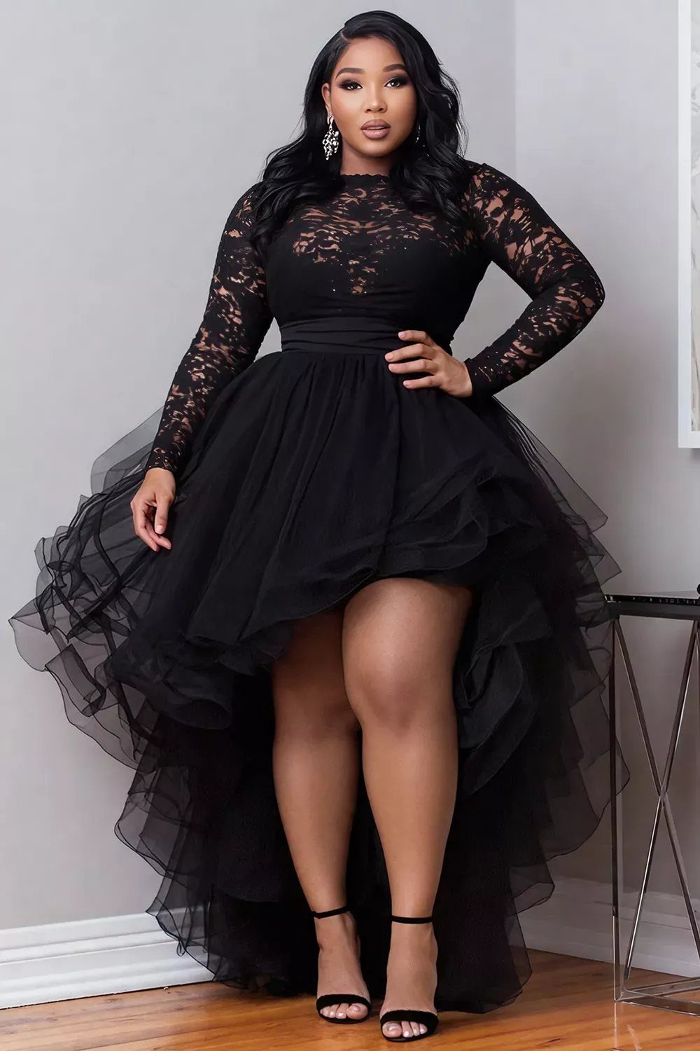 Woman wearing a black lace high-low dress with a voluminous tulle skirt.