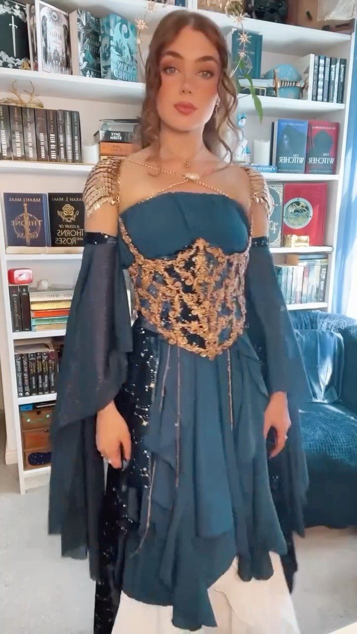 Woman in a teal and gold fantasy dress standing before a bookshelf.