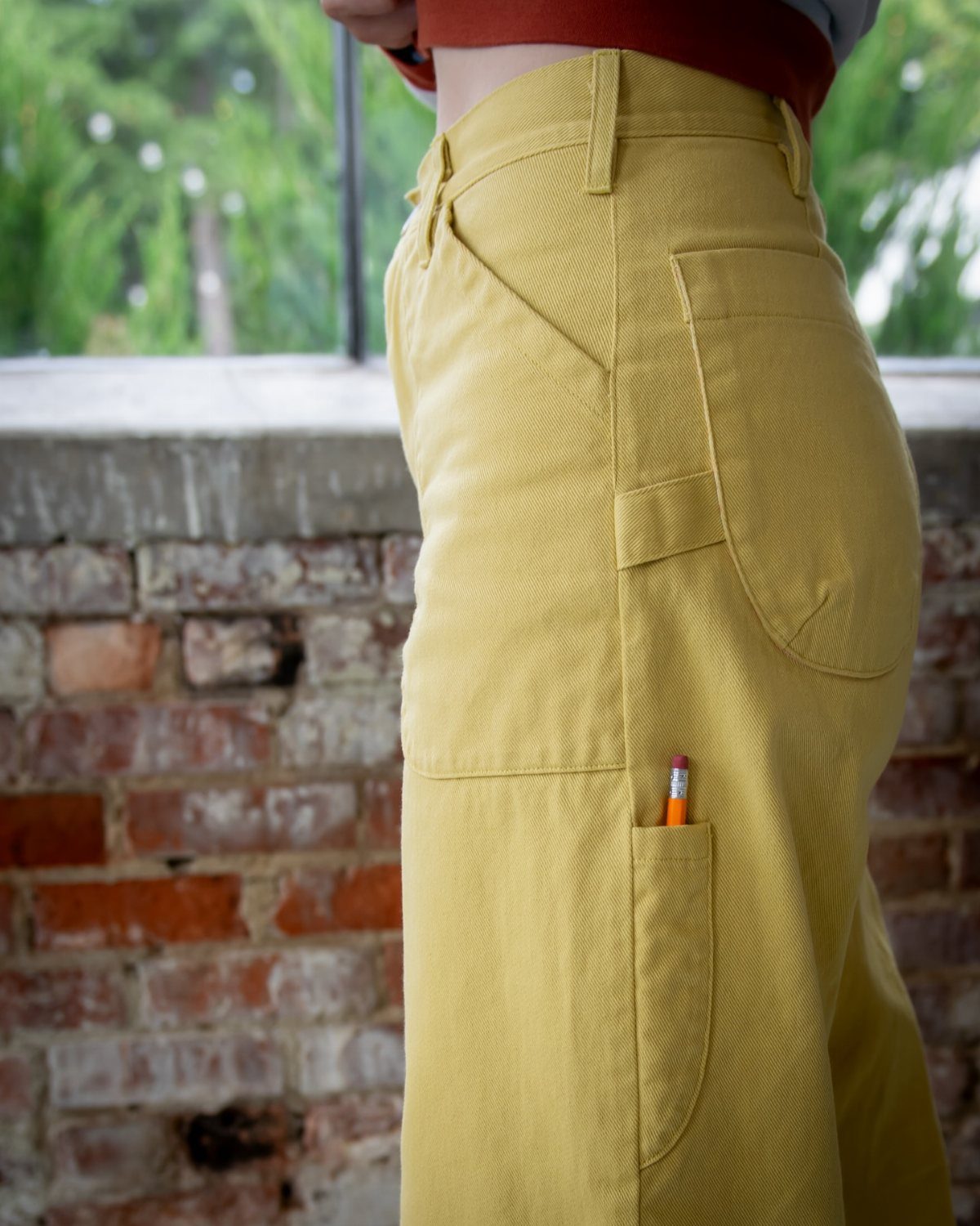 Yellow canvas work pants with deep pockets and a pencil tucked inside.