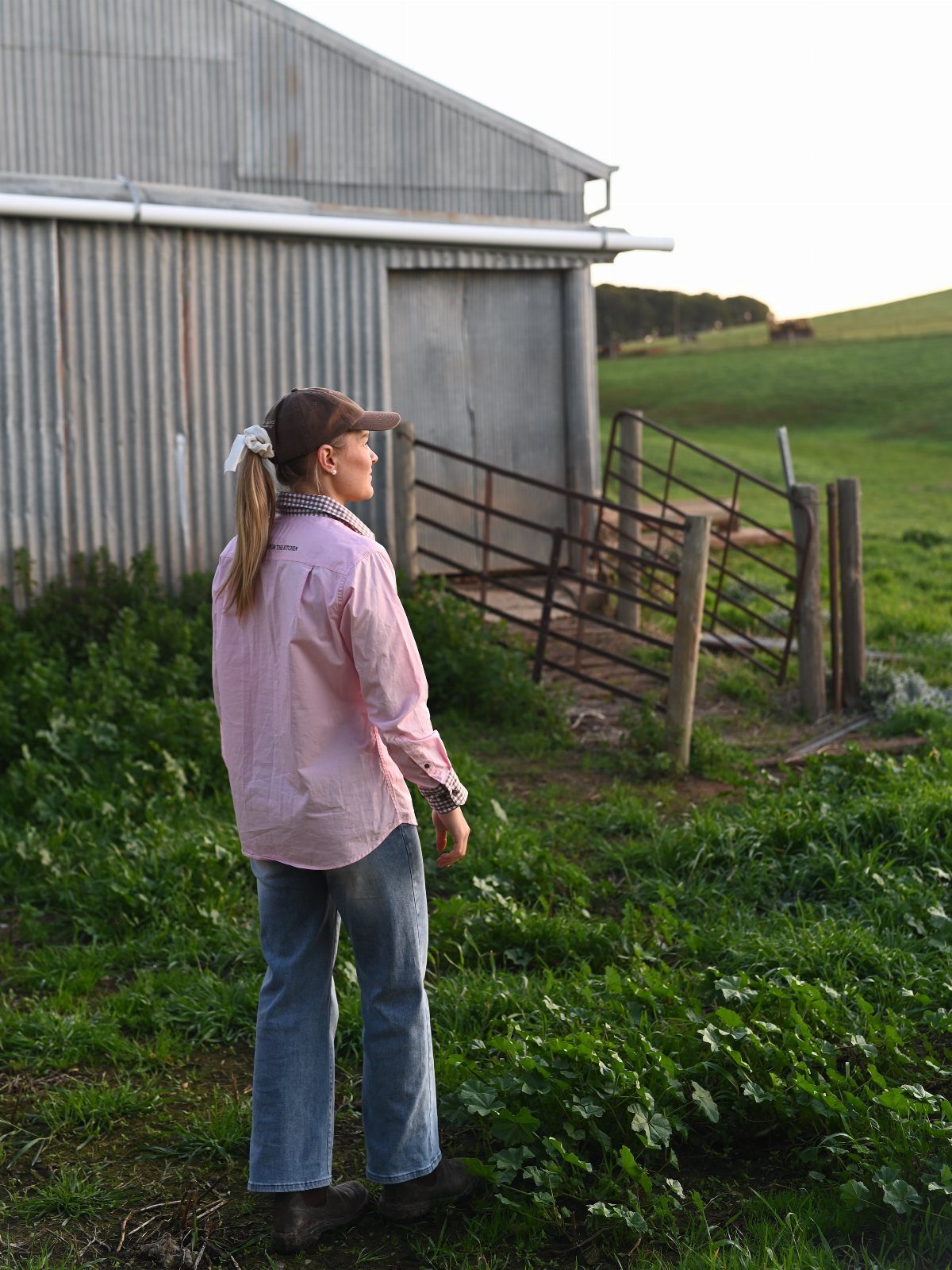 Woman in pink shirt and blue jeans standing by a farm barn.