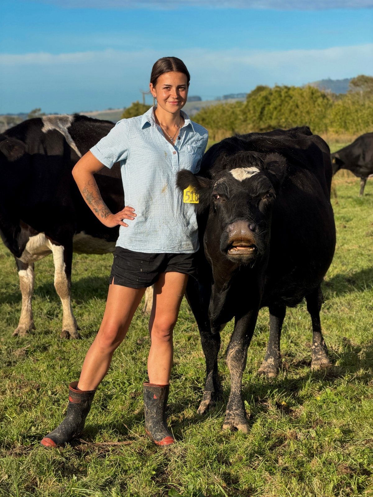 Woman in checkered shirt and rubber boots standing with cows in a field
