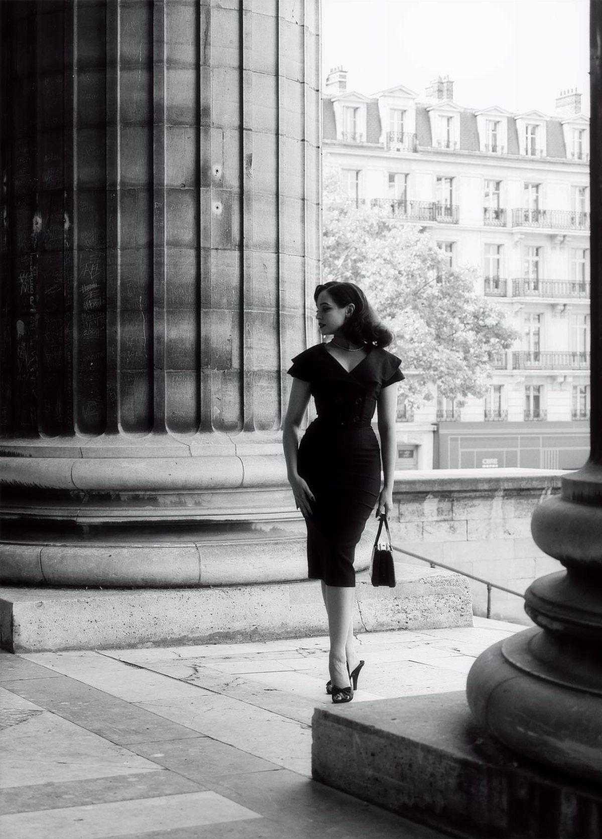 Femme Fatale 1940s Style: 5 Ideas from Film Noir 4 Woman in a black vintage dress posing between large stone columns in Paris.