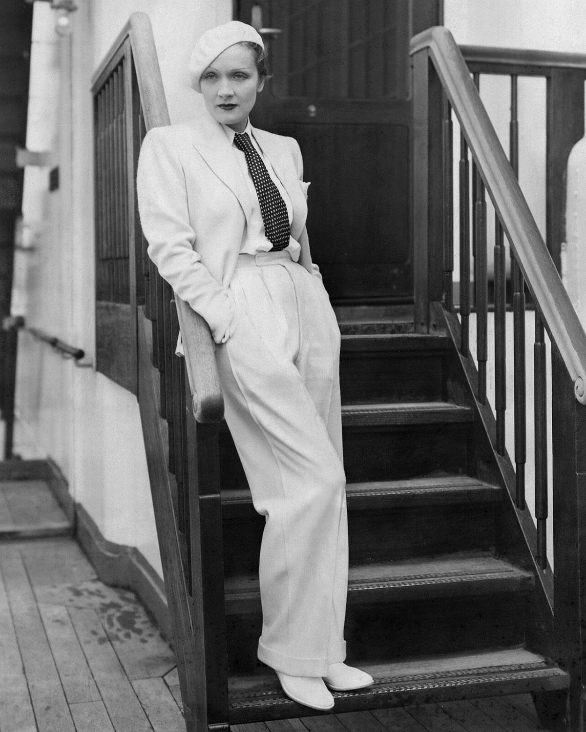 Femme Fatale 1940s Style: 5 Ideas from Film Noir 5 Woman in a 1940s light-colored suit and hat posing on wooden stairs.