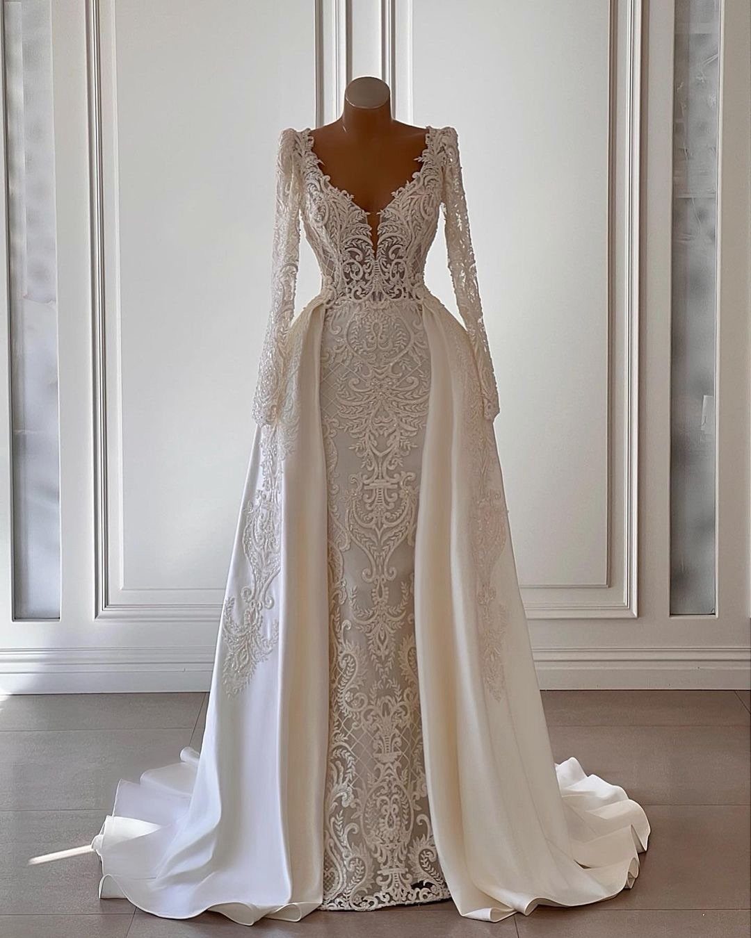 White lace wedding dress with long sleeves and a flowing overskirt on mannequin