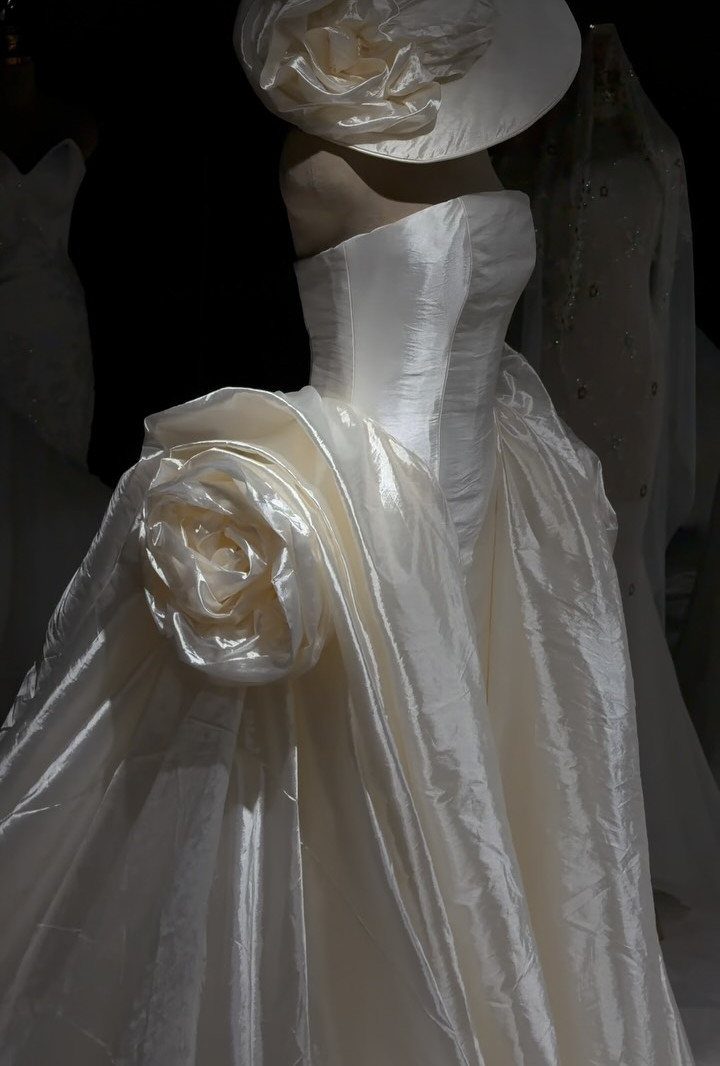 White satin wedding dress on a mannequin with large fabric rose decorations.