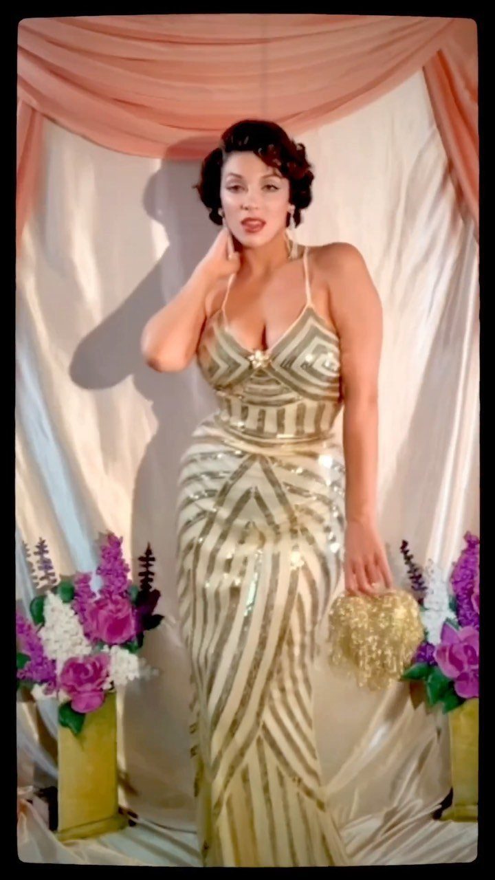 Woman in a gold sequined gown posing against a draped fabric backdrop.