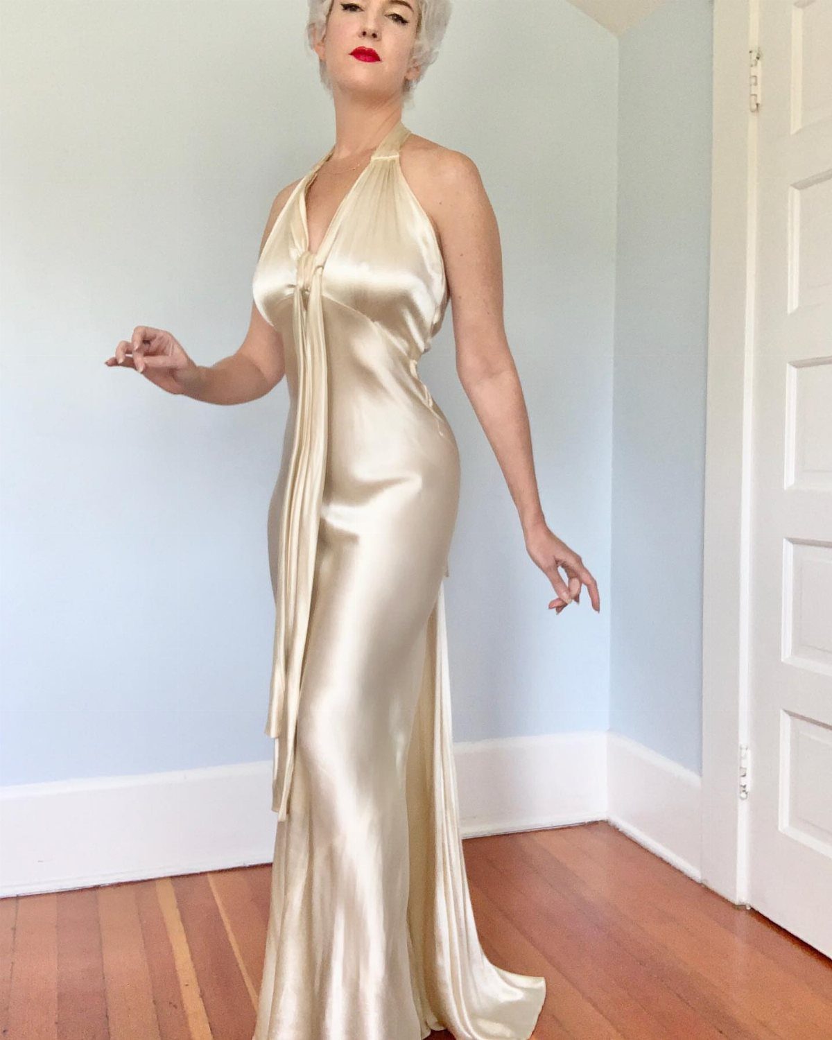 Woman wearing a champagne satin column dress with a halter neckline and draped detail.