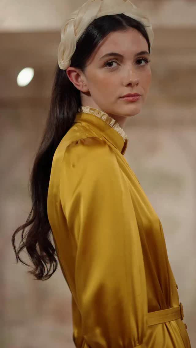 Woman wearing a gold satin dress and cream headband in a classic style.