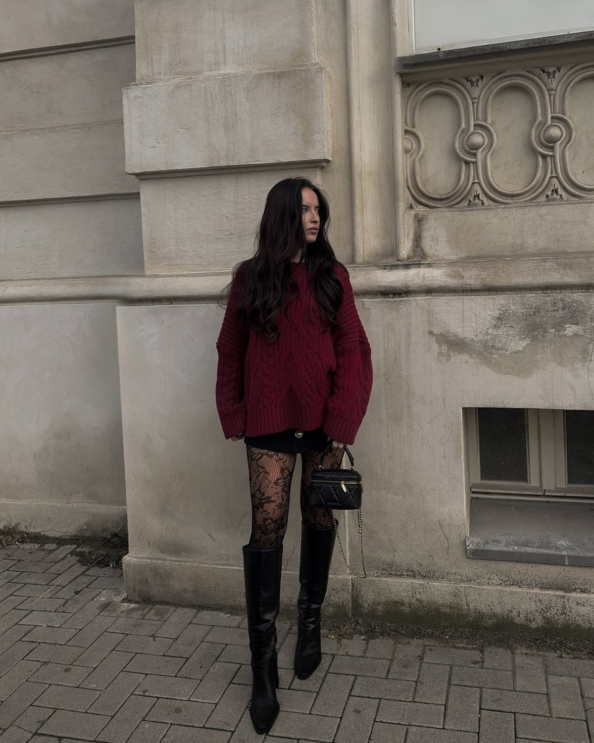 Woman wearing burgundy sweater, black lace tights, and tall black leather boots.