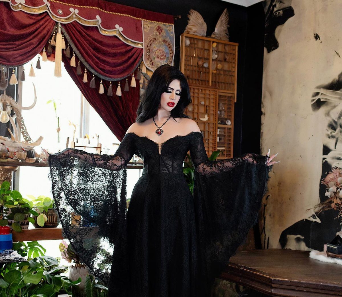 Woman in a black lace off-the-shoulder romantic goth dress standing in a vintage room.
