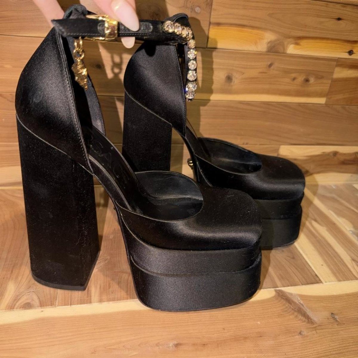 Black satin platform heels with crystal and gold charm embellishments on ankle straps.