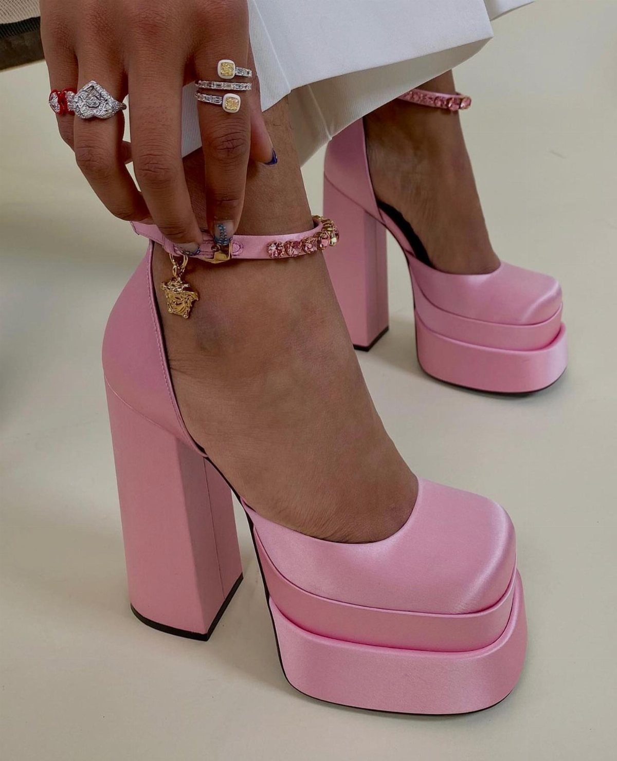 Pink satin platform heels with gold charms on the ankle strap.
