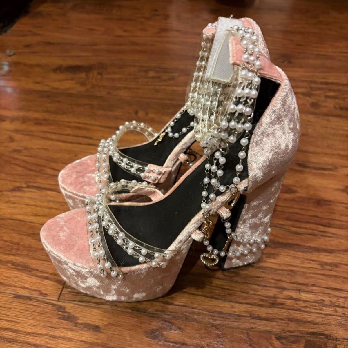 Pink velvet platform heels adorned with pearl chains and gold charms on wood.