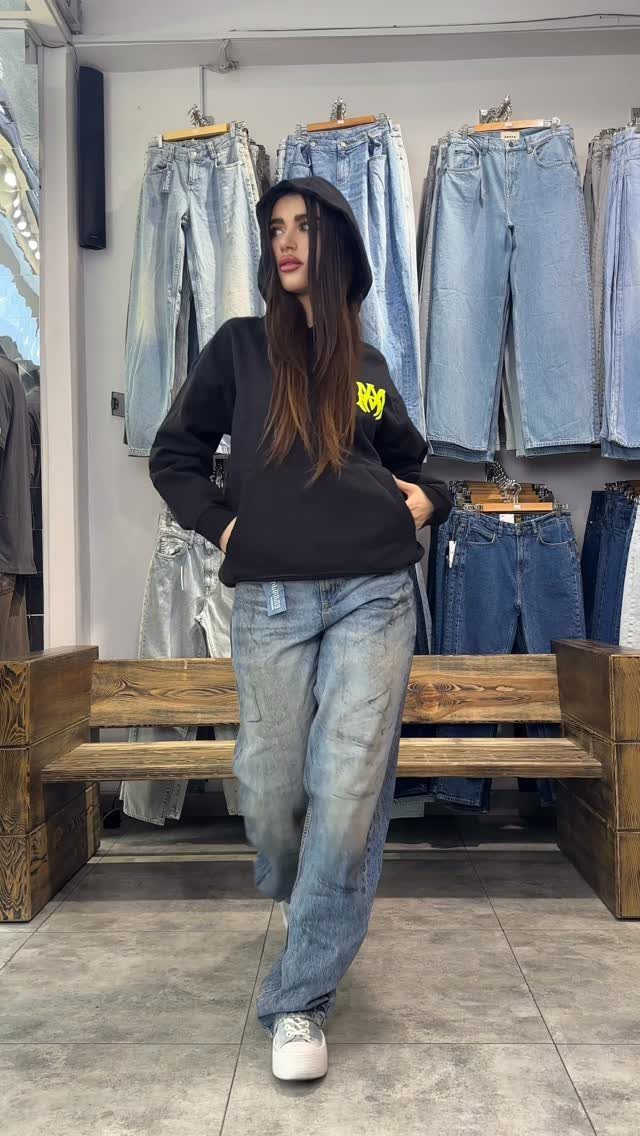 Woman wearing a black hoodie and light-wash baggy jeans in a denim store.