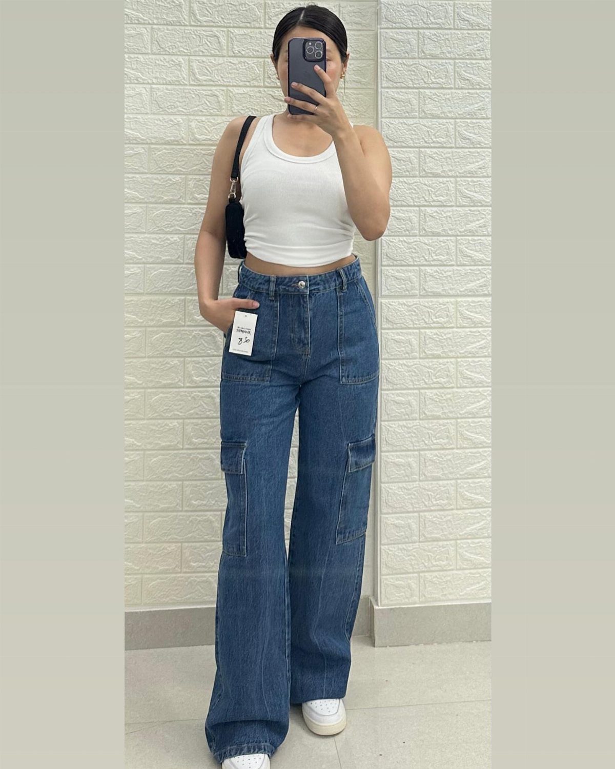 Person wearing white cropped tank top and high-waisted blue cargo baggy jeans.