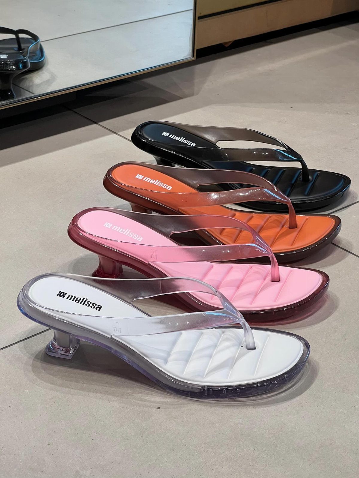 Four pairs of Melissa jelly kitten heel sandals in various colors on a floor.