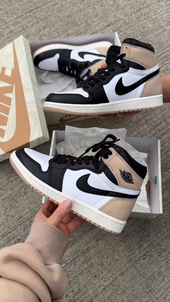 High-top Jordan sneakers in white, black, and tan held over shoe boxes.