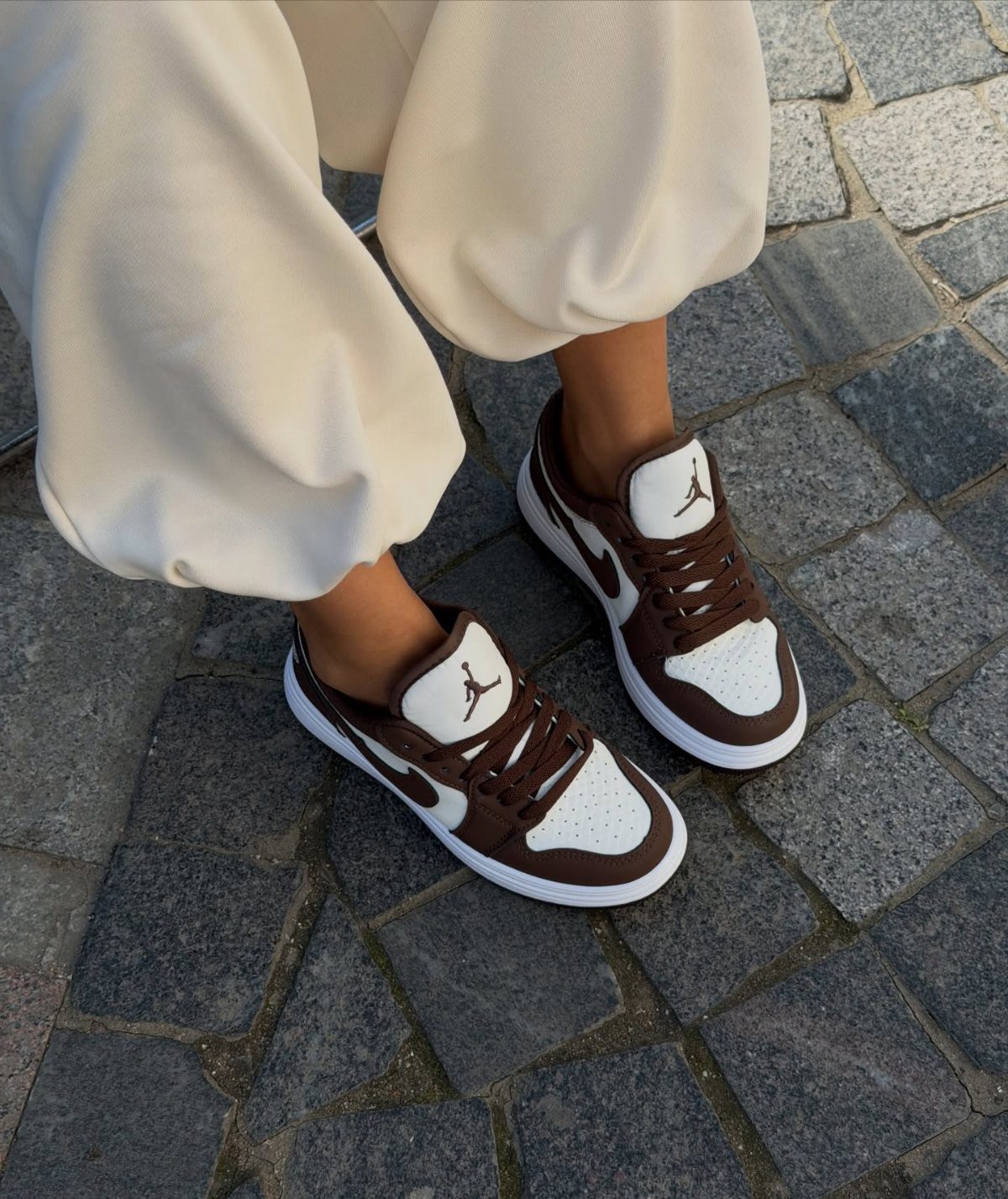 Brown and white Jordan sneakers worn with cream trousers on cobblestone street.