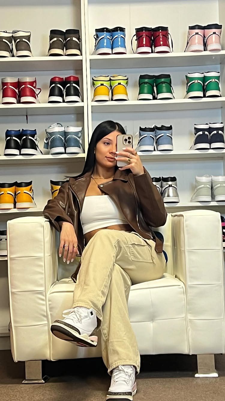 Woman in brown leather jacket and beige cargo pants wearing white Jordan sneakers.