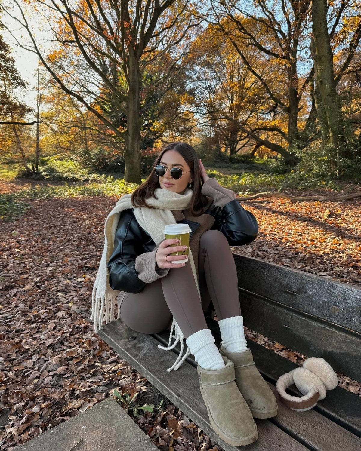 Leggings and Ugg Boots: 6 Outfit Ideas for Cold Days 2 Woman in black biker jacket, brown leggings, and tan Ugg boots sitting outdoors.
