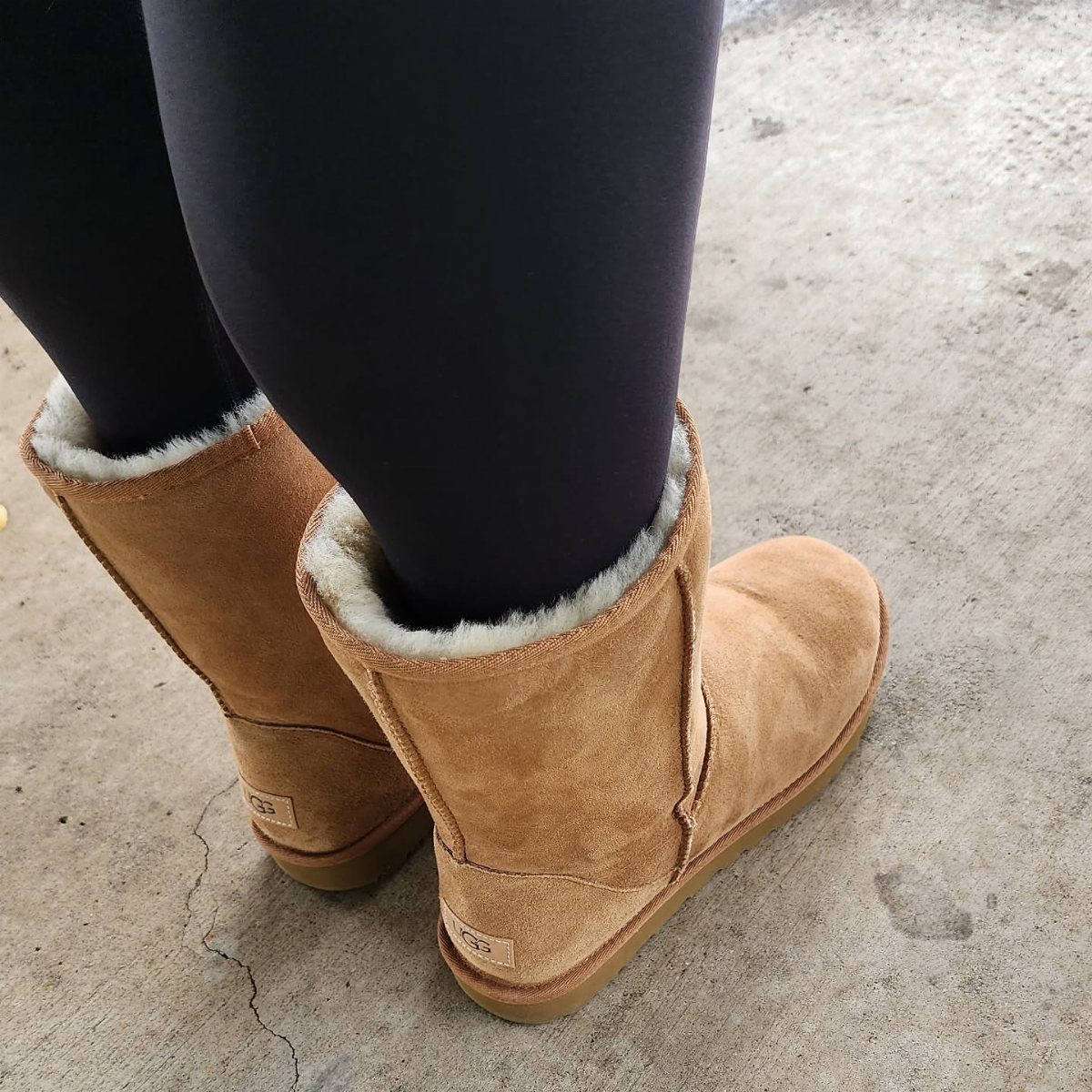 Leggings and Ugg Boots: 6 Outfit Ideas for Cold Days 6 Black leggings and tan suede Ugg boots standing on a grey concrete floor.