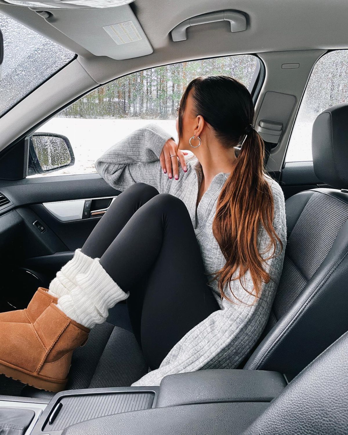 Leggings and Ugg Boots: 6 Outfit Ideas for Cold Days 1 Woman in a grey oversized sweater, black leggings, and tan Ugg boots in a car.