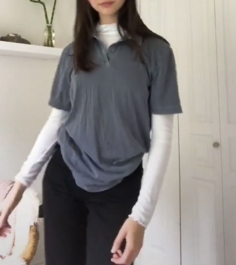 Person wearing a grey short-sleeved polo shirt over a white long-sleeved shirt.