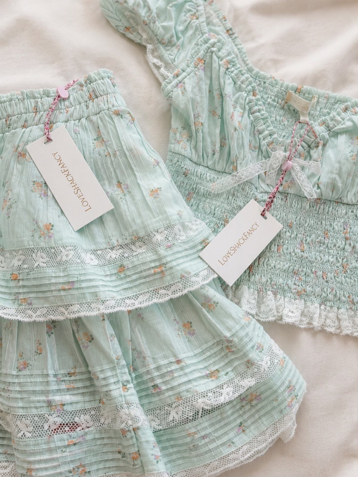 Mint green floral two-piece set with lace trim and ruffles laid on white fabric.