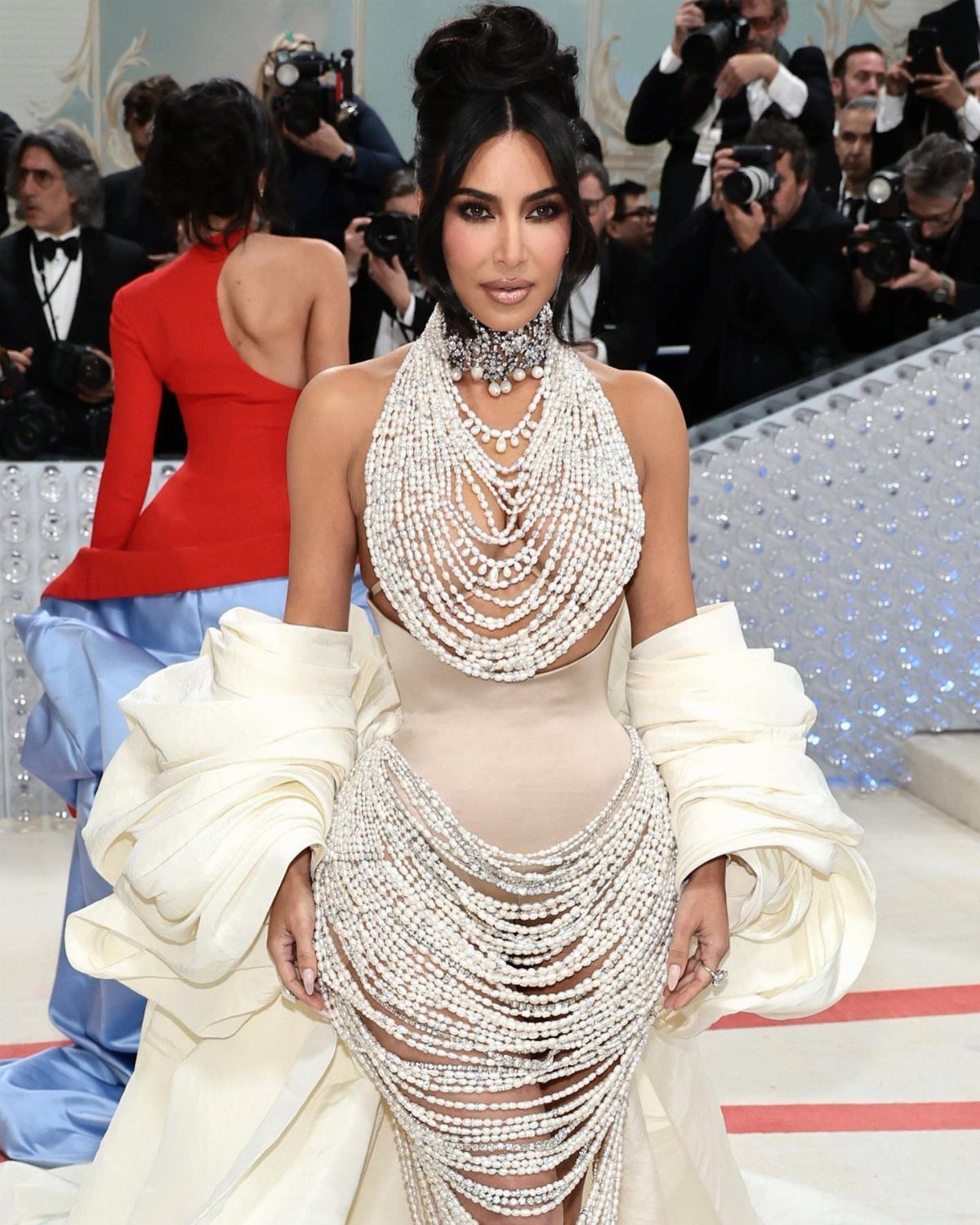 Woman in a white pearl-covered avant-garde gown posing on a red carpet.