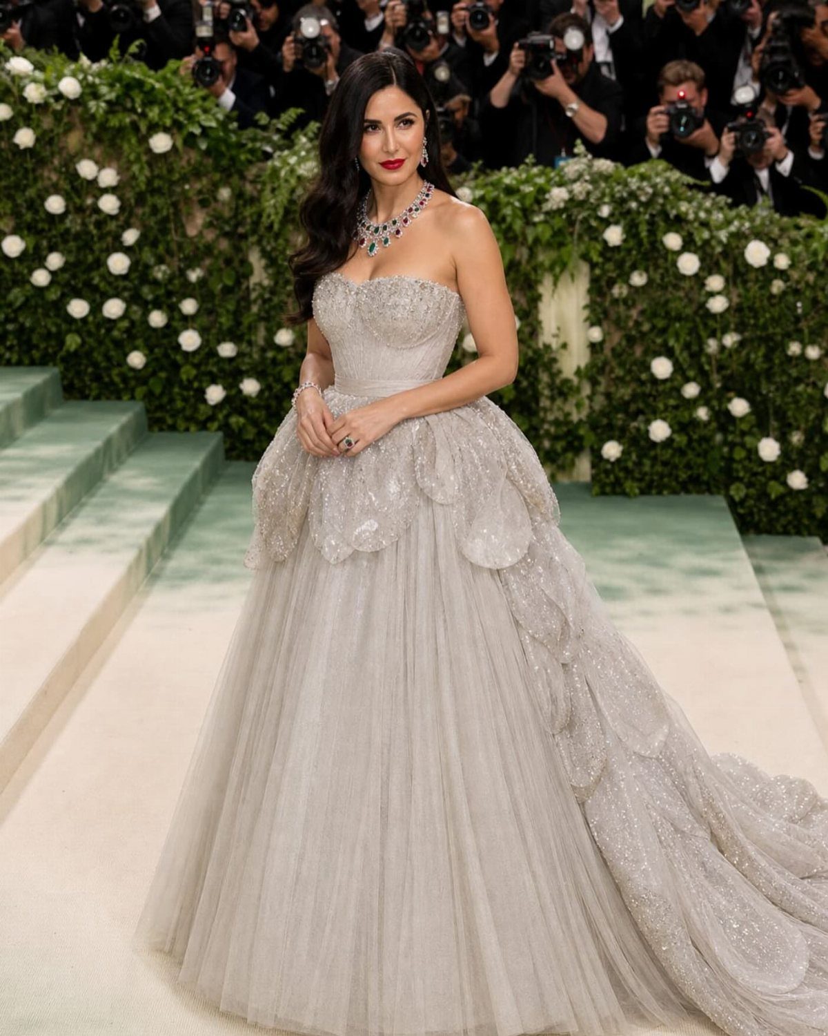 Woman in a shimmering silver-grey embellished gown standing before a white rose wall.
