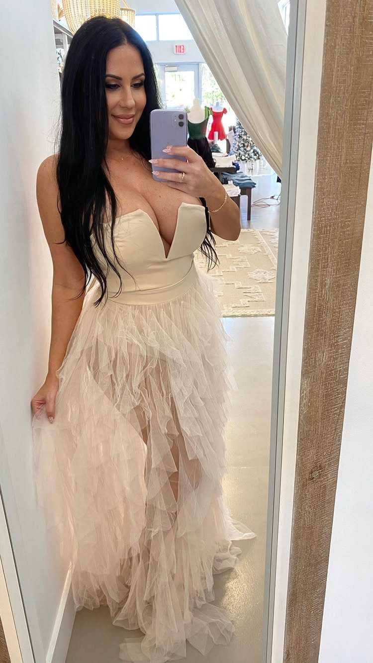 Woman in a strapless tan gown with a ruffled tulle skirt taking a selfie.