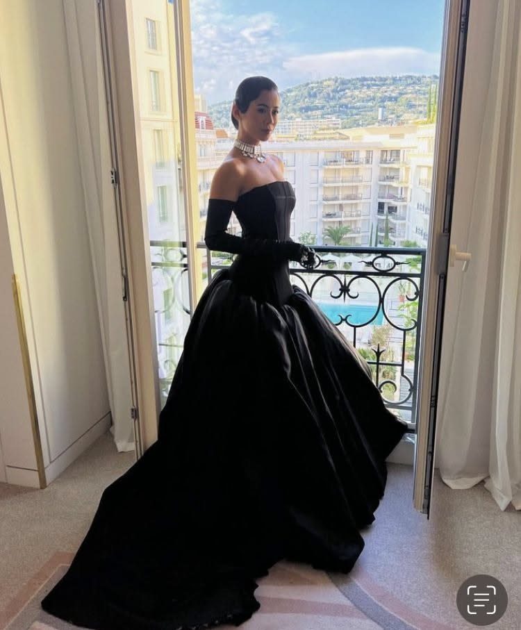 Woman in a strapless black satin gown with matching opera gloves by a balcony.