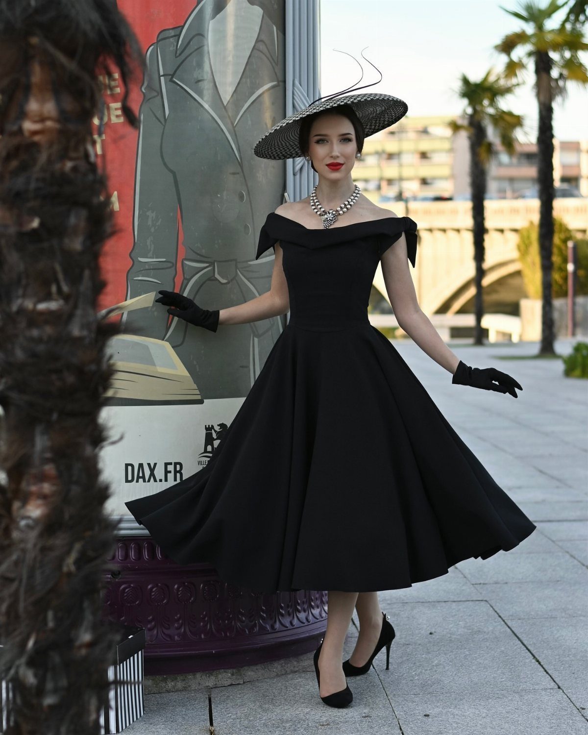 Woman in black off-the-shoulder midi dress with full skirt and wide-brimmed hat.