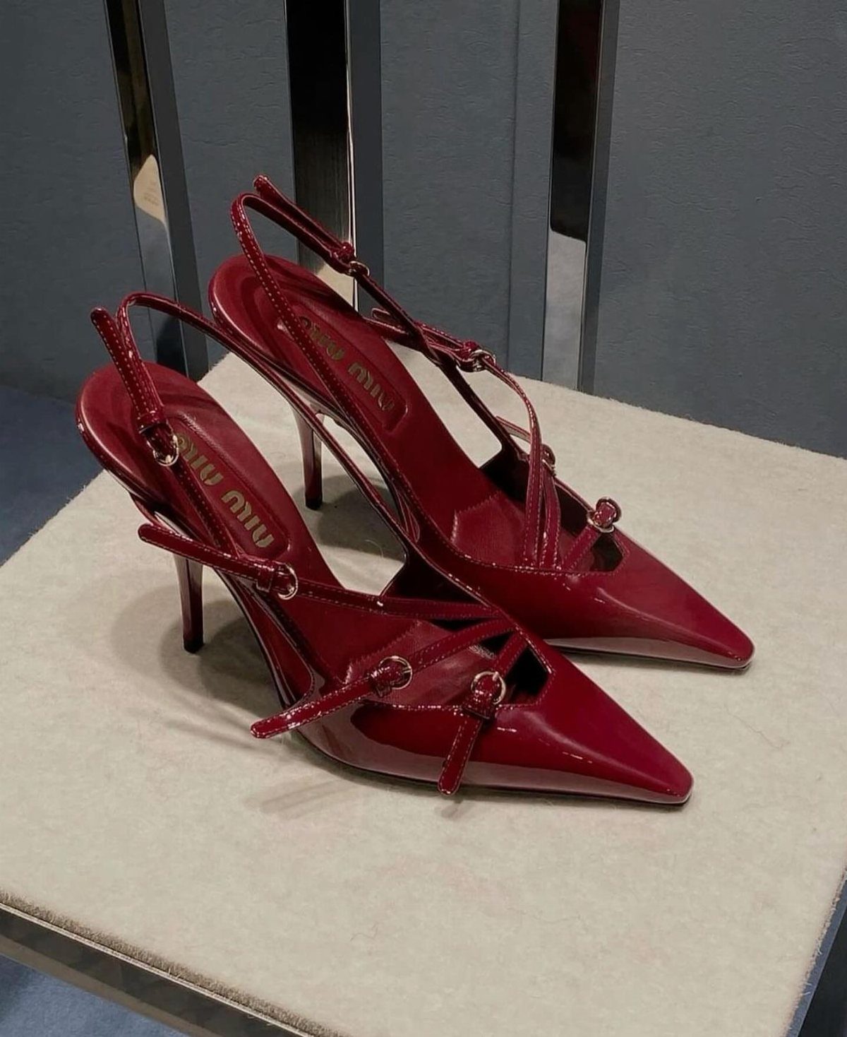 Burgundy patent leather pointed-toe heels with thin ankle straps on a light surface.