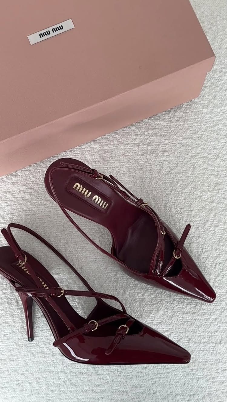 Burgundy patent leather pointed-toe heels with thin straps next to a pink shoebox.