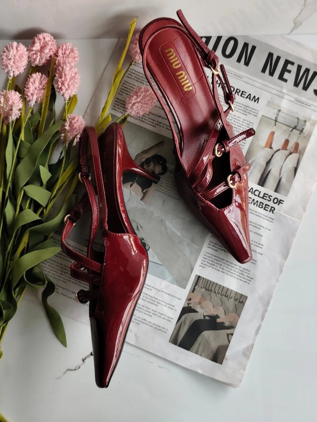 Burgundy patent leather slingback heels with pointed toes on a newspaper and flowers.