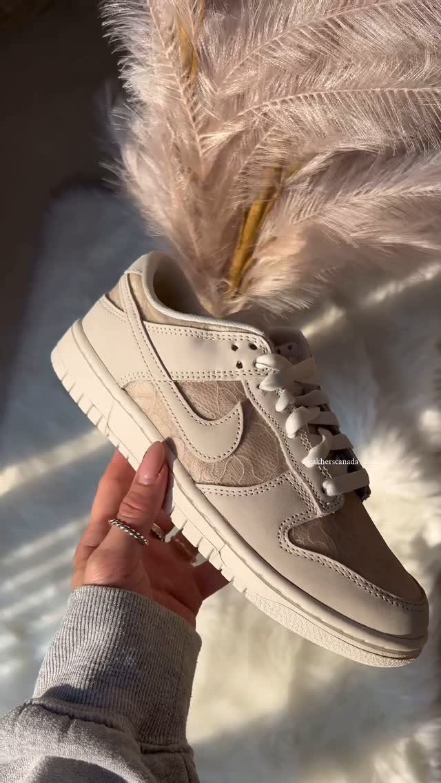 Beige leather sneaker held by a hand against a soft, fluffy background.