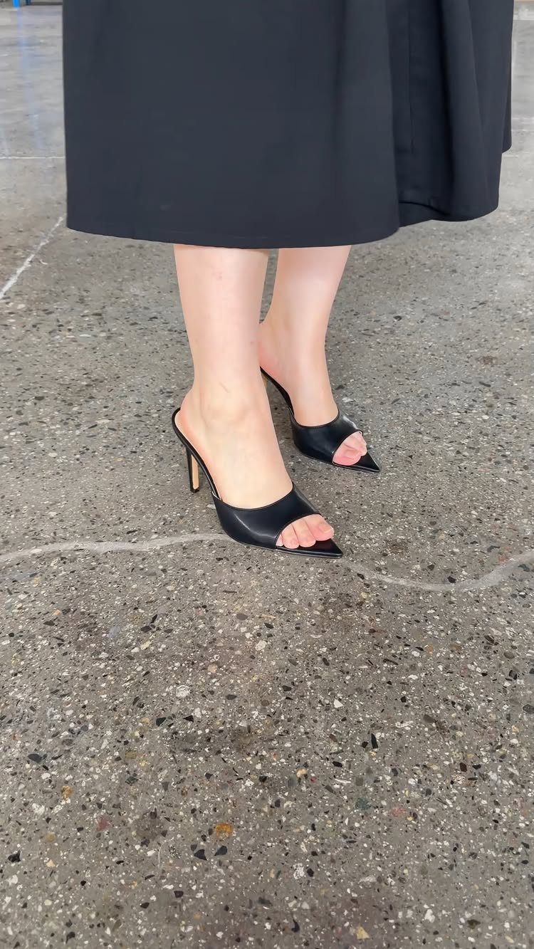 Black open-toe high-heel mules with a high vamp worn with a black skirt.