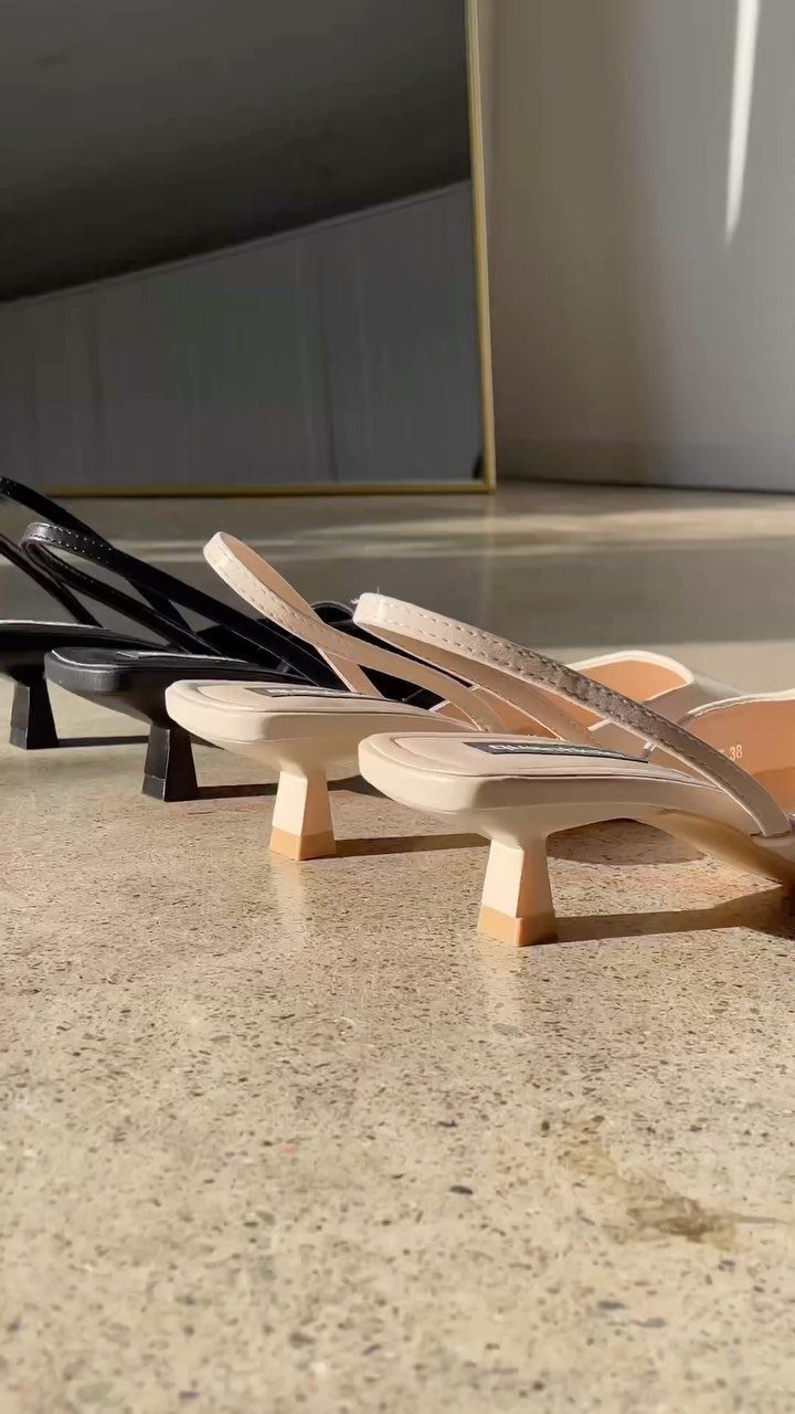 Kitten heel mules in black and beige tones lined up on a stone floor.