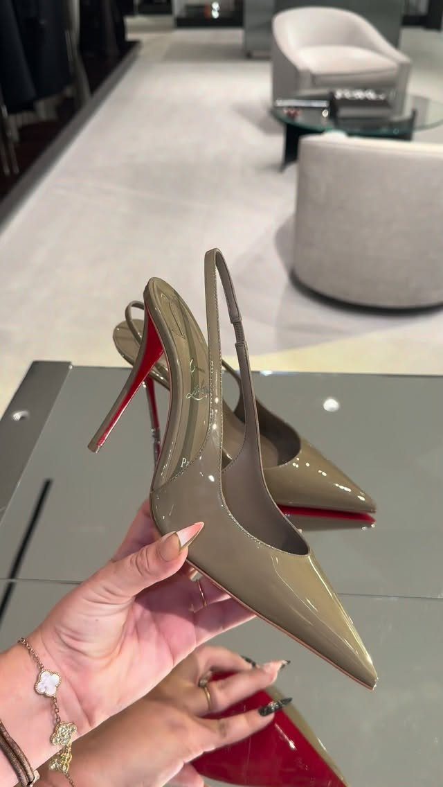 Taupe pointed-toe high heels with red soles held by a hand in a store.