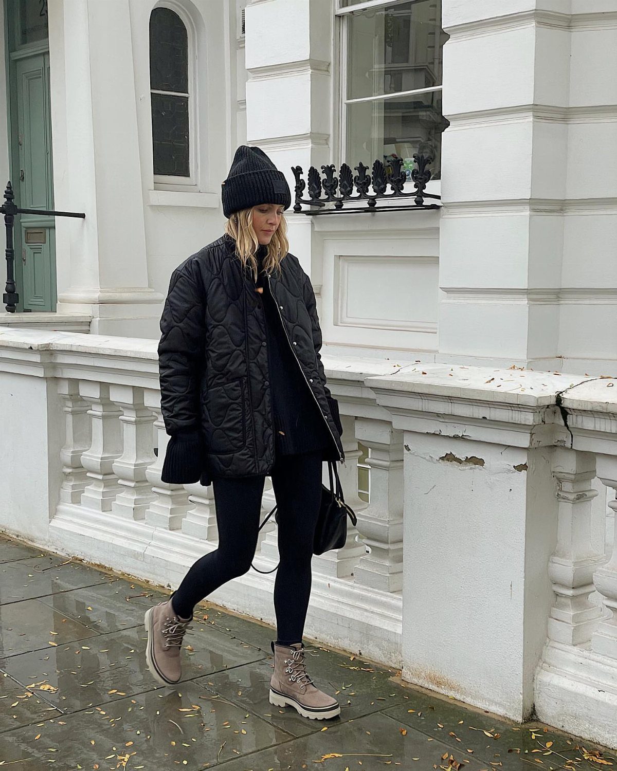 Woman wearing tan weather-friendly boots and black winter clothes walking on wet pavement.