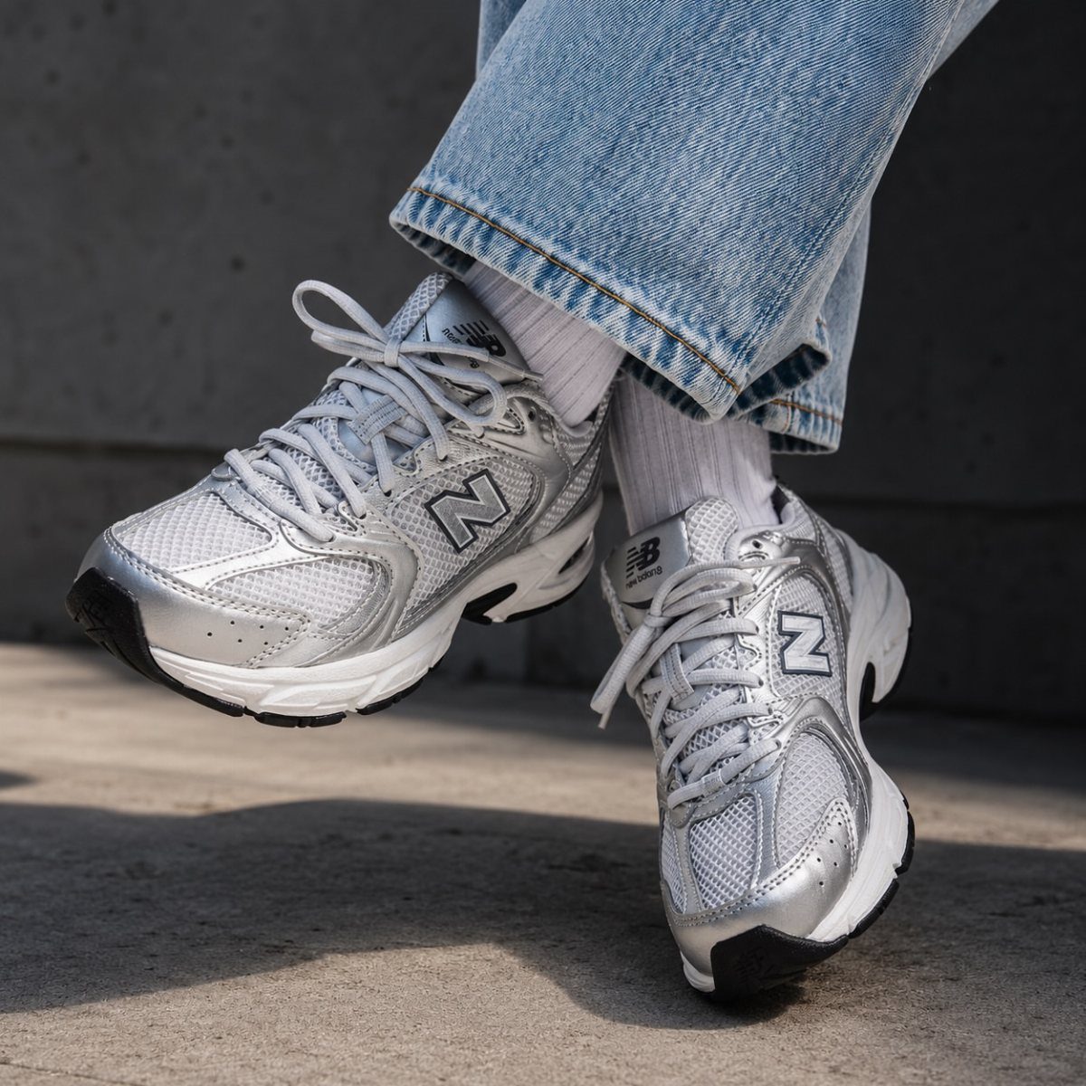 Silver and white New Balance 530 sneakers worn with blue jeans and white socks.