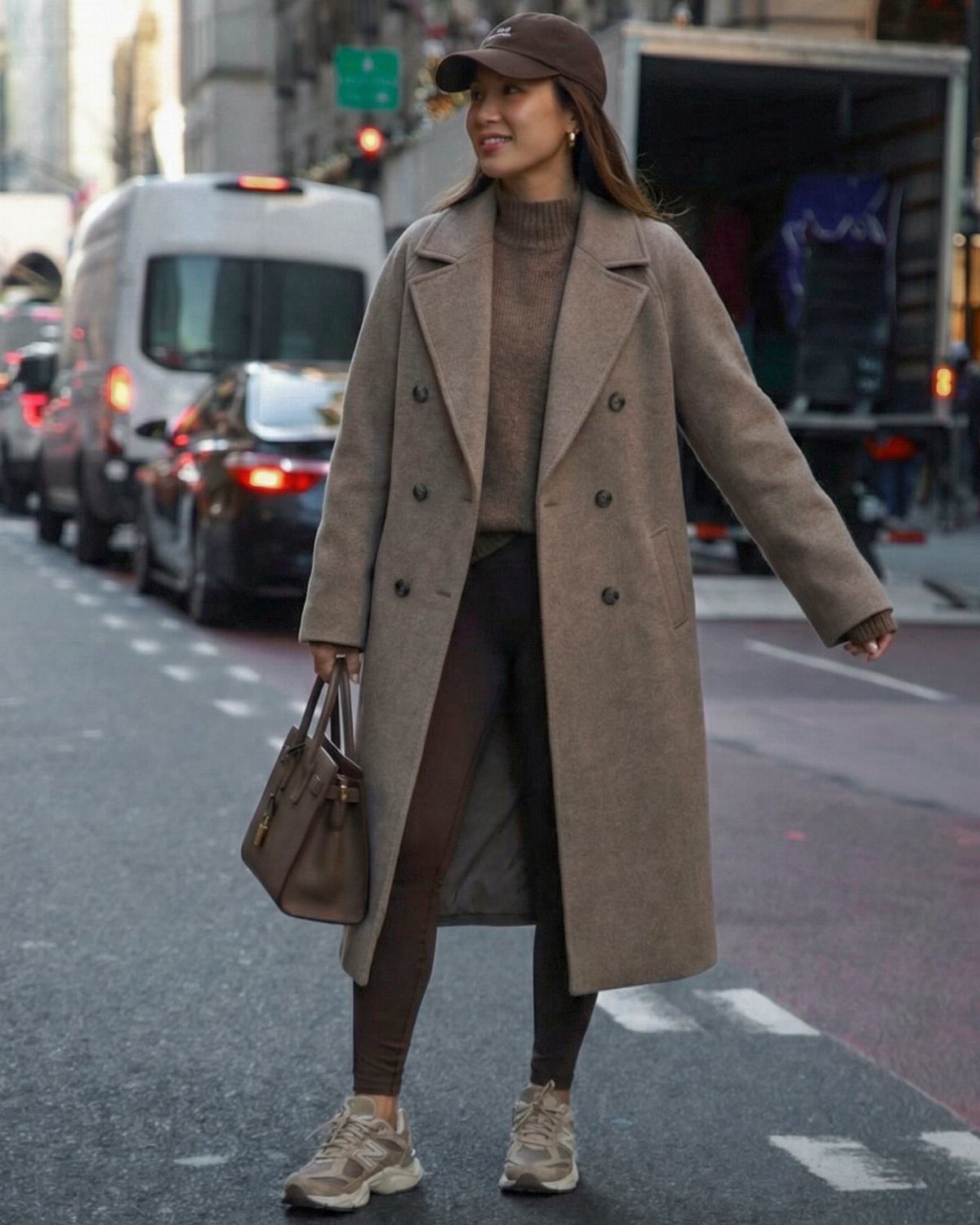 Woman in oversized brown coat and leggings wearing beige New Balance 9060 sneakers.
