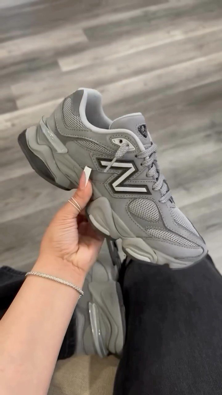 Grey New Balance 9060 sneaker held by a hand over black pants.