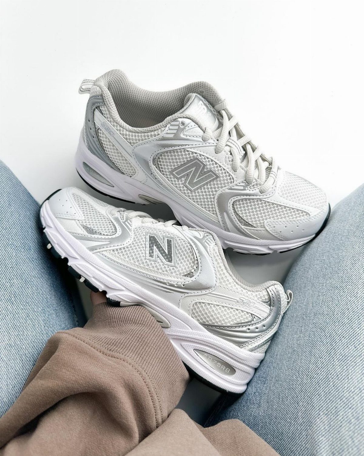 White and grey New Balance 9060 sneakers worn with light blue denim jeans.