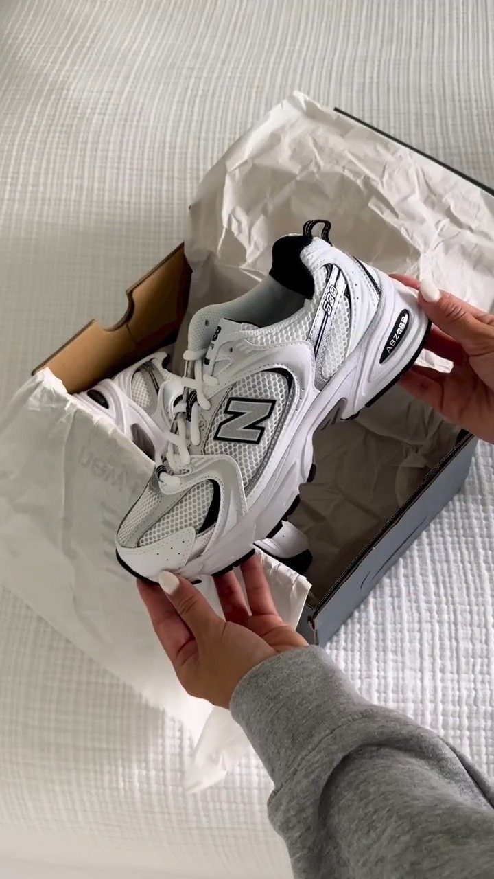 White New Balance 530 sneaker held over an open shoebox on white fabric.