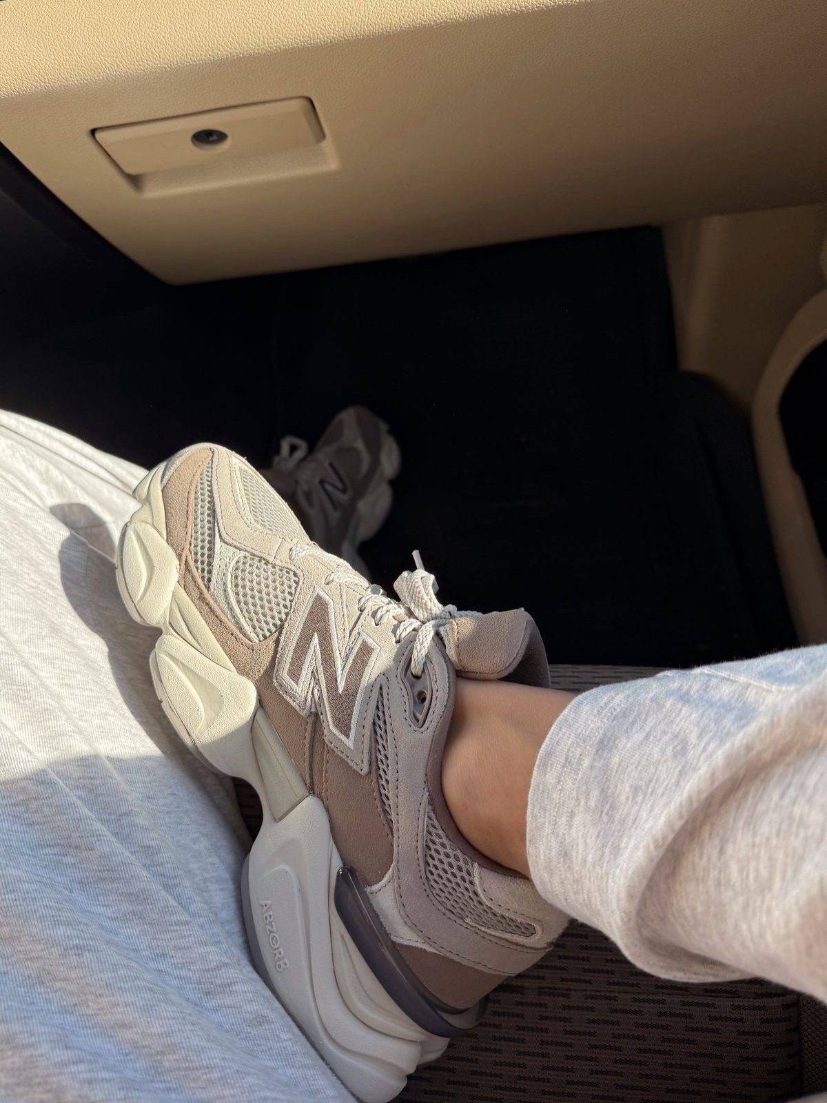Beige New Balance 9060 sneakers worn with grey sweatpants inside a car.